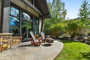 Een huis met grote ramen, een stenen muur en een terras met twee Adirondack-stoelen en een vuurkorf.