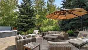 Un espace extérieur aménagé en terrasse, avec des meubles en osier, un grand parasol et un barbecue.