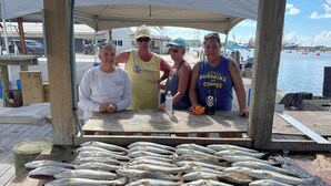 A wooden dock with a table displaying fresh fish and three people standing behind it.
