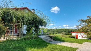 Ett hus på landsbygden med ett rött tak, omgivet av frodig grönska och en klarblå himmel.