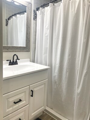 A bathroom with a white sink, black faucet, and a white shower curtain.