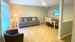 Un vaste espace de vie comprenant un canapé gris, une table à manger avec des chaises, une lampe et un téléviseur fixé au mur.