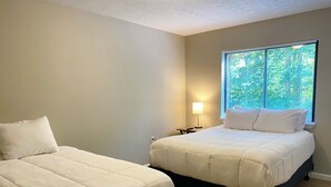 Une chambre avec deux lits, une table de chevet, une lampe et une fenêtre avec des stores.