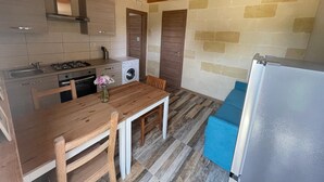 Eine kleine Küche mit Holztisch, Stühlen, einer Waschmaschine und einem Kühlschrank.