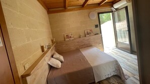 Ein Schlafzimmer mit Holzboden, einem Bett mit weißer und brauner Bettdecke, einem kleinen Nachttisch und einem Fenster mit Blick auf Grün.