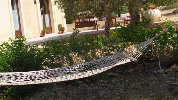 Eine Hängematte in einem Garten, im Hintergrund ein Gebäude.