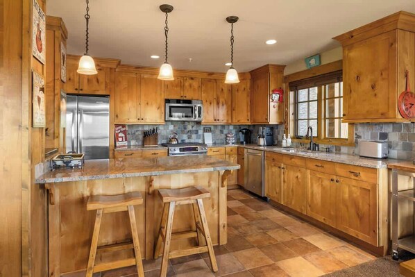 A kitchen with wooden cabinets, a central island with stools, stainless steel appliances, and pendant lighting.