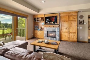 A cozy living room with a fireplace, a television mounted on a wooden wall, and a balcony with a view of the outdoors.