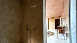 Un baño moderno con ducha, puerta de vidrio que da a una sala de estar y techo de madera.