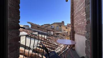 Un balcón con una pequeña mesa y sillas, con vista a un patio que tiene una pared de ladrillo y un edificio al fondo.