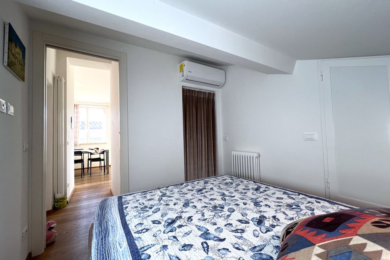 Un dormitorio con cama, un radiador, un equipo de aire acondicionado y una puerta que da a otra habitación.