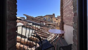 Un balcon avec une petite table et des chaises, donnant sur une cour intérieure bordée d’un mur de briques et sur laquelle on aperçoit un bâtiment au fond.