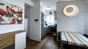 Une cuisine moderne avec des meubles blancs, un coin repas doté d’une table à rayures et un mur orné d’un tableau représentant un flamant rose.