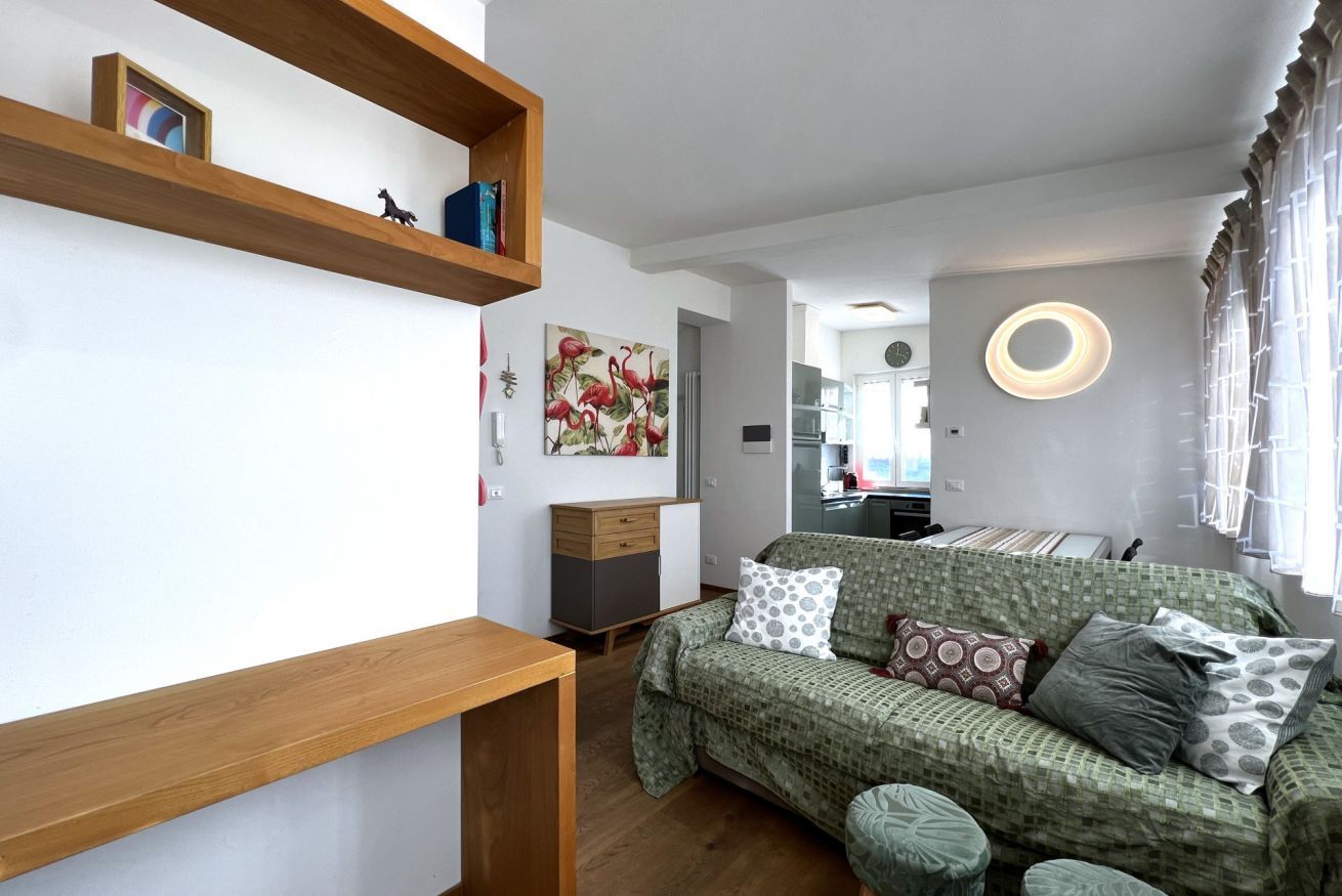 A cozy room with a green patterned sofa, wooden shelves, and a circular light fixture.