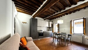 Una sala de estar acogedora con un sofá, una mesa de comedor con sillas, una zona de cocina con armarios y electrodomésticos, y un ventanal con cortinas.