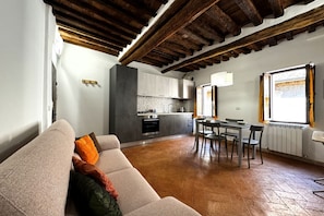 A cozy living room with a sofa, a dining table with chairs, a kitchen area with cabinets and appliances, and a window with curtains.