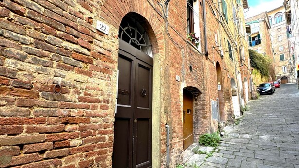 Una estrecha calle adoquinada con un edificio de ladrillo que presenta un gran arco de entrada y una placa con un número.