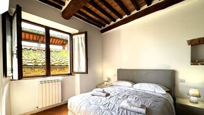 Un dormitorio con una cama grande, una ventana con vistas a un jardín, un radiador y vigas de madera en el techo.