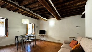 Una sala de estar con un sofá, una mesa de comedor con sillas, un televisor sobre un mueble bajo y una chimenea.