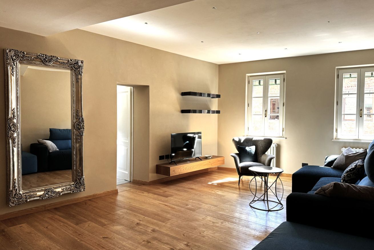 A spacious living room with a large ornate mirror, a flat-screen TV on a wooden stand, a black leather armchair, and a blue sofa.
