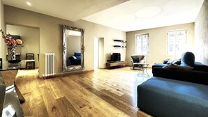 Un soggiorno spazioso con un grande specchio, pavimento in legno, un divano blu e una televisione.