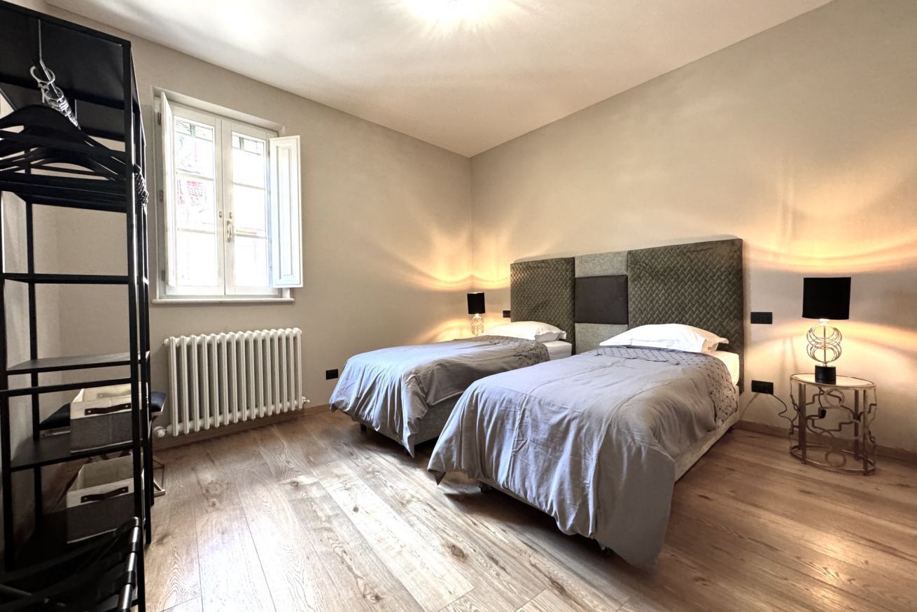 Una habitación con dos camas, un radiador, una ventana y una estantería negra.