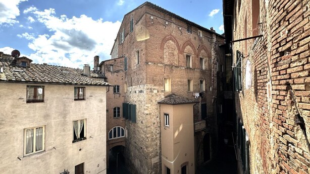 Un stretto vicolo tra edifici dall'architettura tradizionale, tra cui un edificio in mattoni con finestre ad arco e un edificio più piccolo con tetto in tegole.