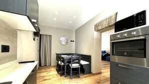 Una cucina compatta con forno integrato, una zona pranzo con tavolo e sedie, e una sveglia appesa al muro.
