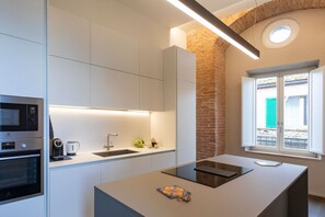 Una cocina moderna con armarios blancos, horno empotrado, cafetera y ventana con vista a la calle.