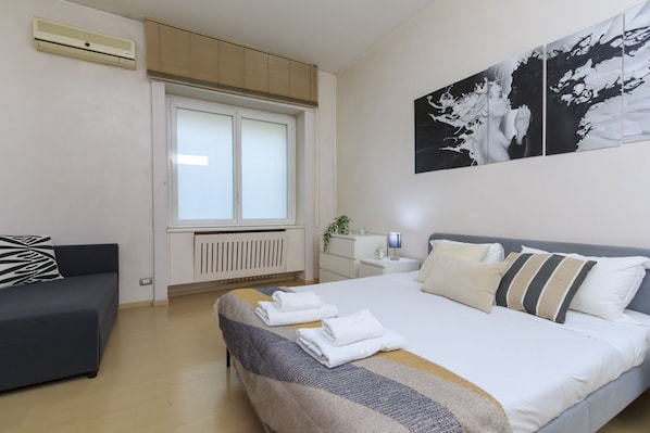 A bedroom with a bed, a sofa, a window, and a radiator.