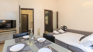 A hotel room with a bed, a TV, a dining table with chairs, and a mirror. - Explore Milan with your family from this spacious and cozy apartment, located just a 15-minute walk from the Duomo! Ideal for families of up to 5 people (plus a crib available upon request), the apartment is equipped with all the comforts you need for a  (Milan)
