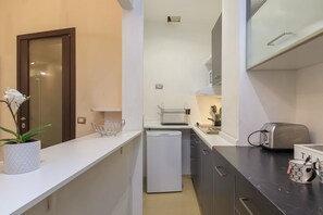 A compact kitchen with a white refrigerator, a toaster, and a coffee maker on the counter. - Explore Milan with your family from this spacious and cozy apartment, located just a 15-minute walk from the Duomo! Ideal for families of up to 5 people (plus a crib available upon request), the apartment is equipped with all the comforts you need for a  (Milan)
