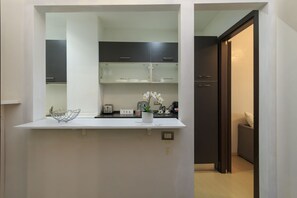 A modern kitchen with white countertops, a coffee machine, and a small plant.