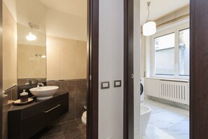 Et moderne badeværelse med et stort spejl, en hvid vask og et toilet.