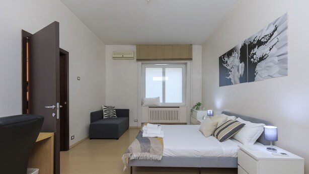 A bedroom with a bed, bedside table, nightstand, and a window with blinds. - Explore Milan with your family from this spacious and cozy apartment, located just a 15-minute walk from the Duomo! Ideal for families of up to 5 people (plus a crib available upon request), the apartment is equipped with all the comforts you need for a  (Milan)