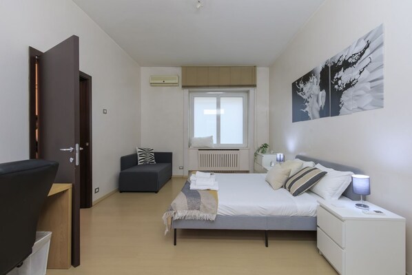 A bedroom with a bed, bedside table, nightstand, and a window with blinds.