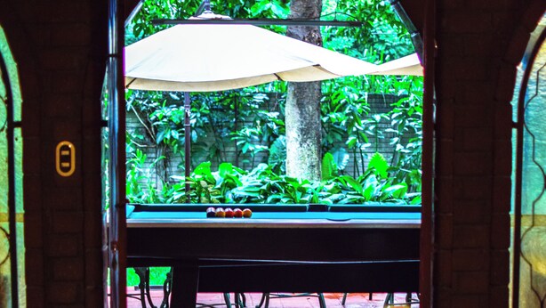 A pool table with a view of a lush garden through a glass door.