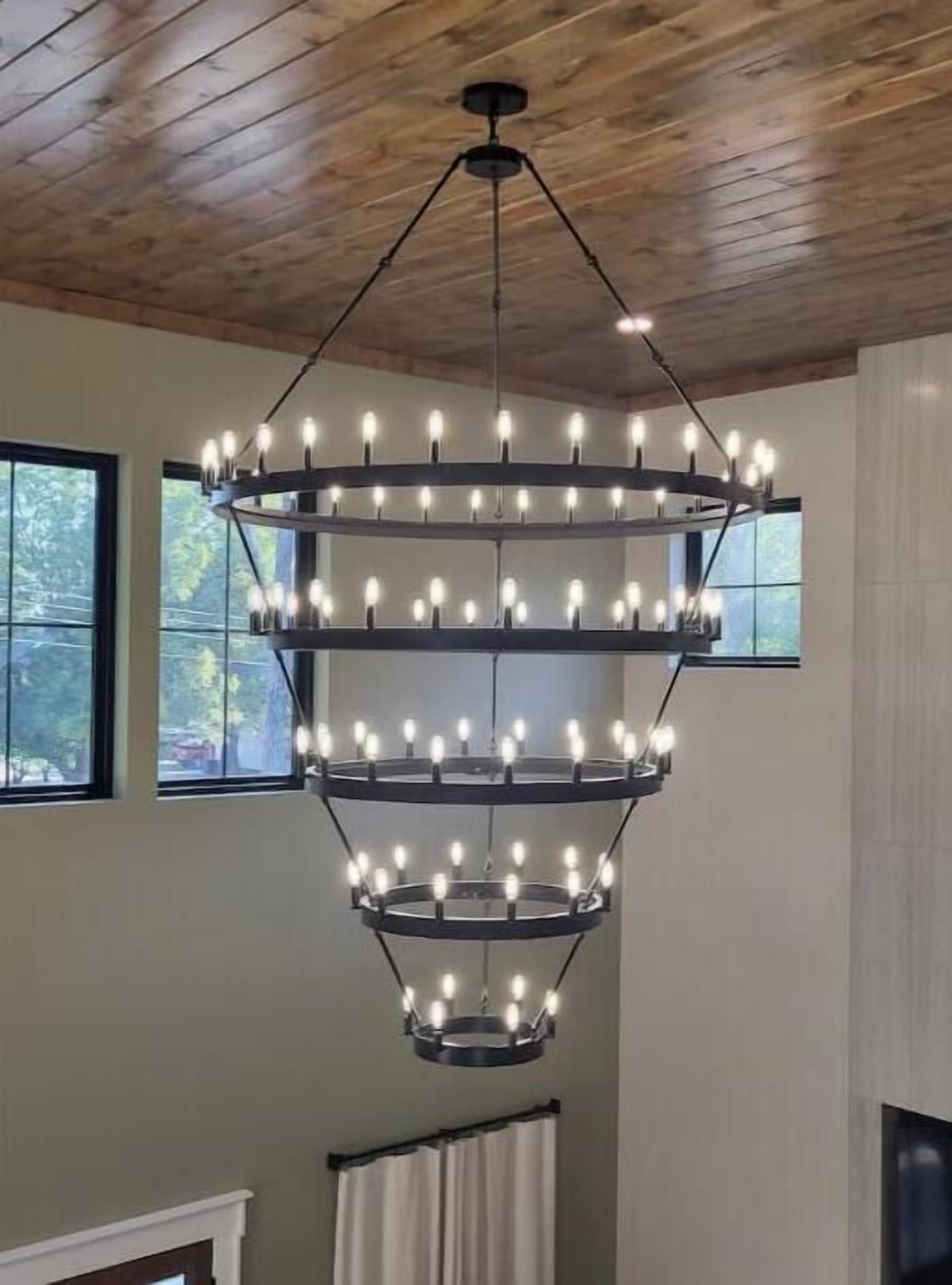A multi-tiered chandelier with multiple bulbs in a room with wooden ceilings and large windows.