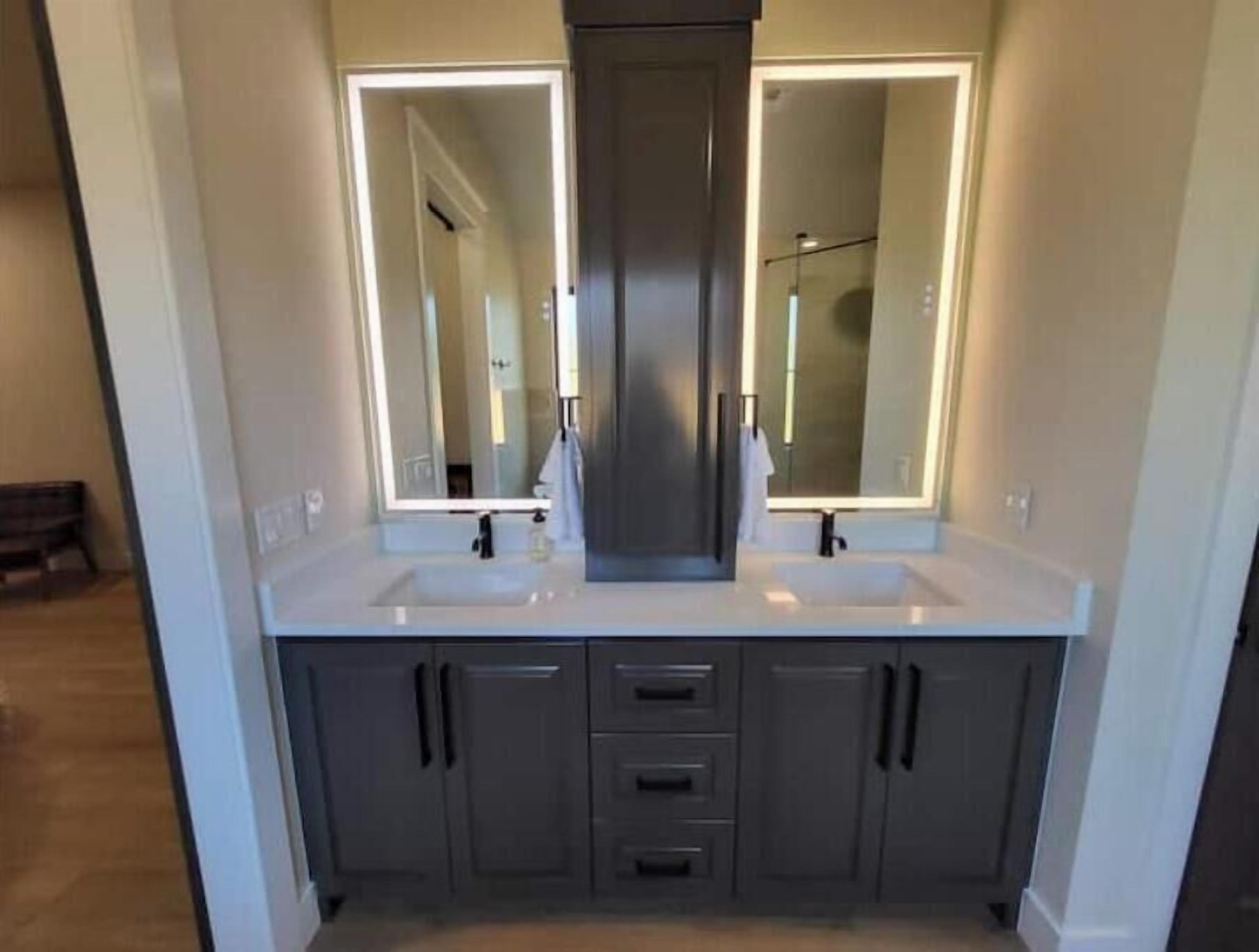 A modern bathroom with two sinks, a large mirror, and a walk-in shower.