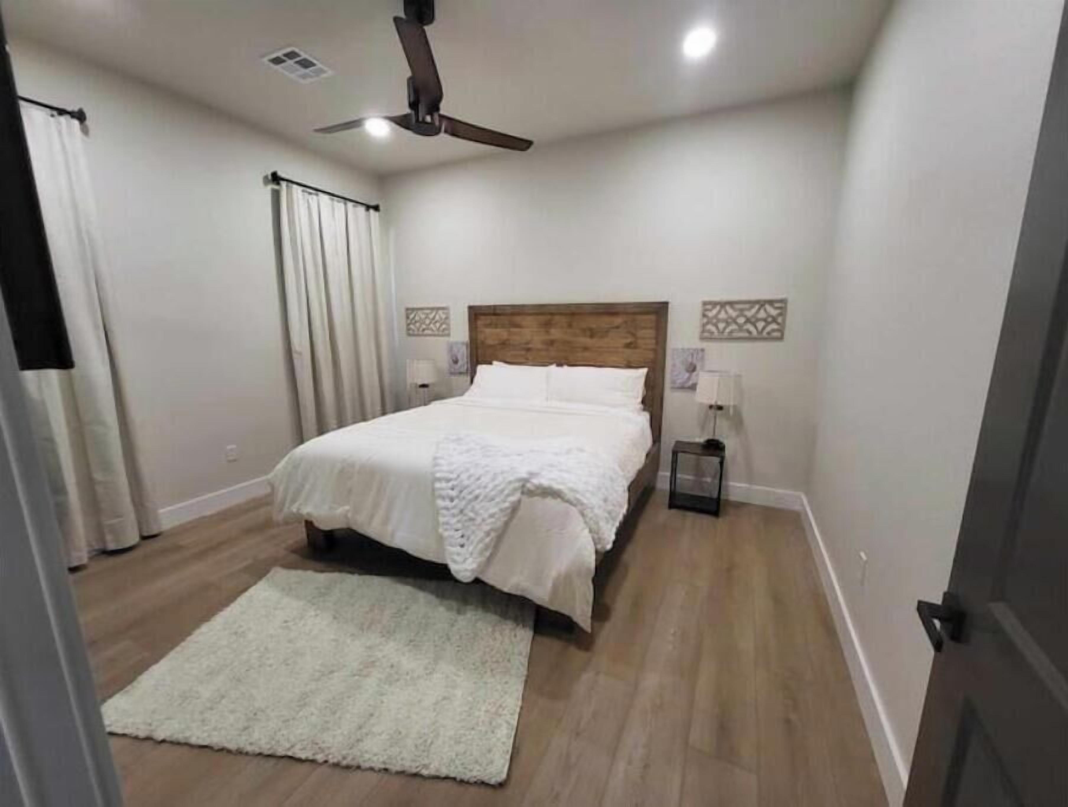 A bedroom with a wooden headboard, a white bedspread, a white rug, and a ceiling fan.