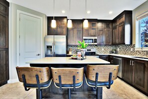 Une cuisine moderne avec des meubles de couleur bois foncé, un îlot central doté de tabourets, un réfrigérateur, un four à micro-ondes et un lave-vaisselle.