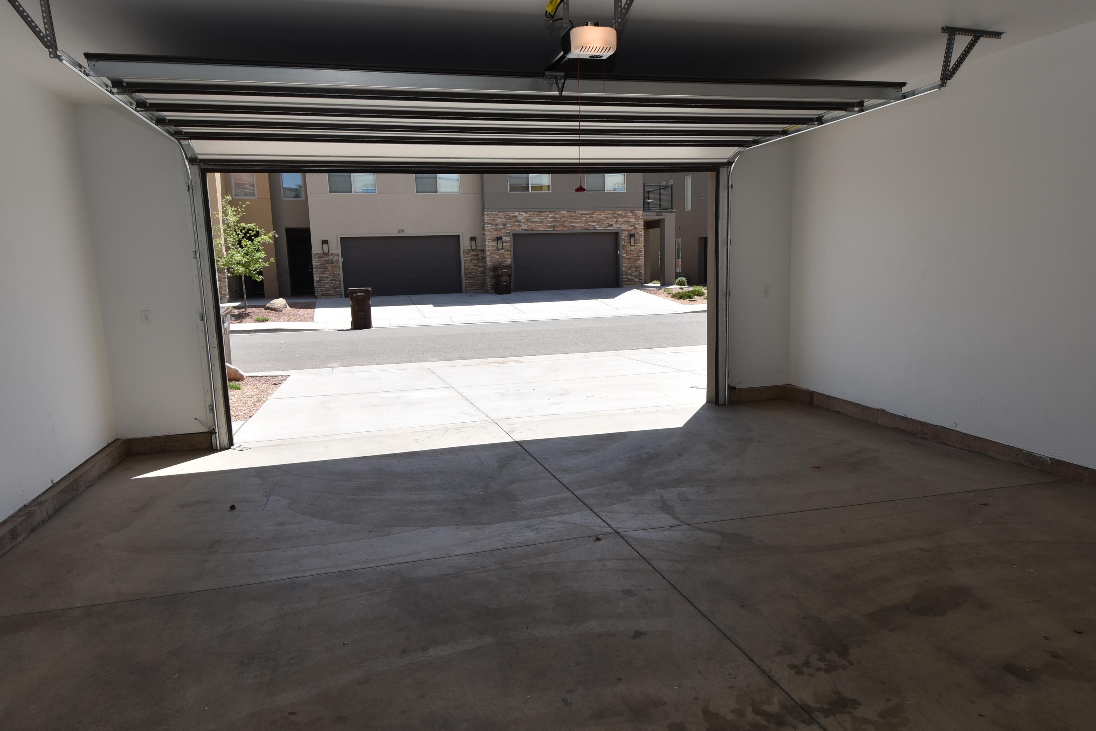 An open garage with a concrete floor, a black garage door, and a view of a street with a building in the background.