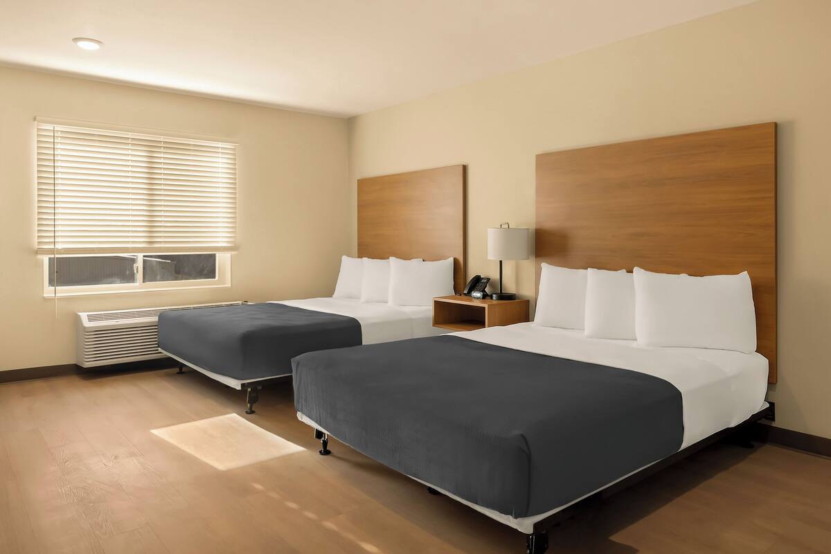 Une chambre d’hôtel avec deux lits, une fenêtre avec des stores, une table de chevet avec une lampe et un téléphone fixé au mur.