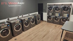 Un cuarto de lavandería con varias lavadoras y secadoras, un letrero que dice 'WASHAWAY' y piso de madera.
