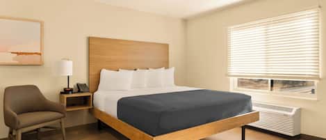 Habitación de hotel con cama de madera, almohadas blancas, mesita de noche con lámpara y ventana con persianas.