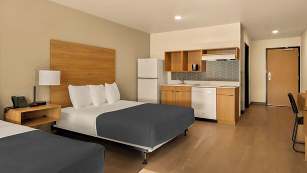 Una habitación de hotel con dos camas, una kitchenette pequeña, un escritorio y una silla.