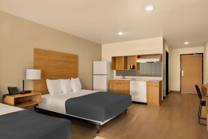 A hotel room with two beds, a small kitchenette, a desk, and a chair.