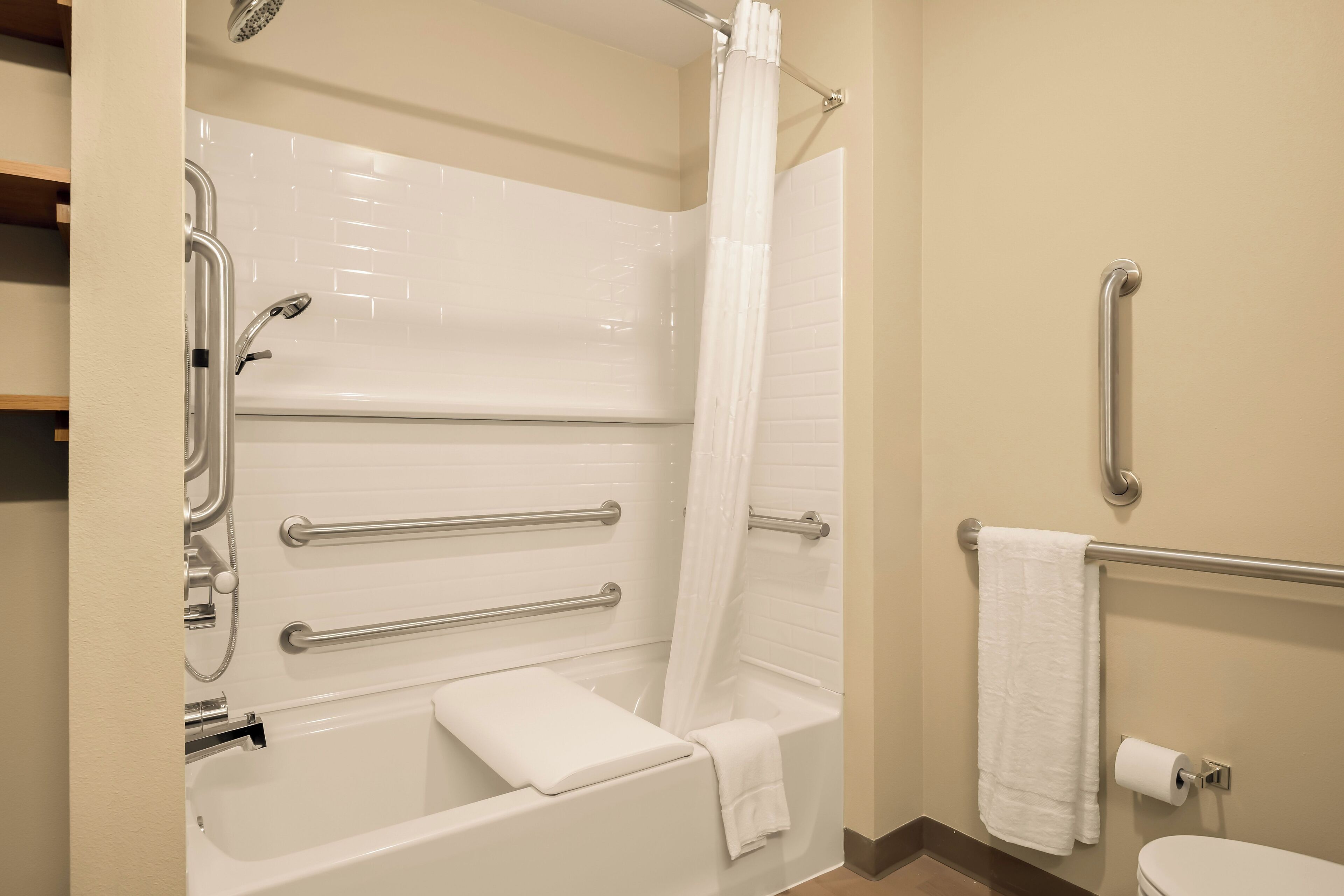 A bathroom with a bathtub, grab bars, a showerhead, a towel rack, and a toilet.