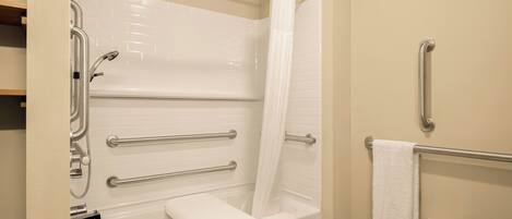 A bathroom with a bathtub, grab bars, a showerhead, a towel rack, and a toilet.