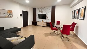 A modern living room with a sofa, a dining table with red chairs, a TV mounted on a marble wall, and a door. - Apartment in San Francisco (Panama City)